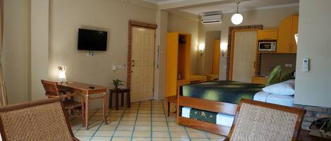 Una habitación de hotel con una cama, un escritorio, dos sillas, un televisor y un ventilador de techo.