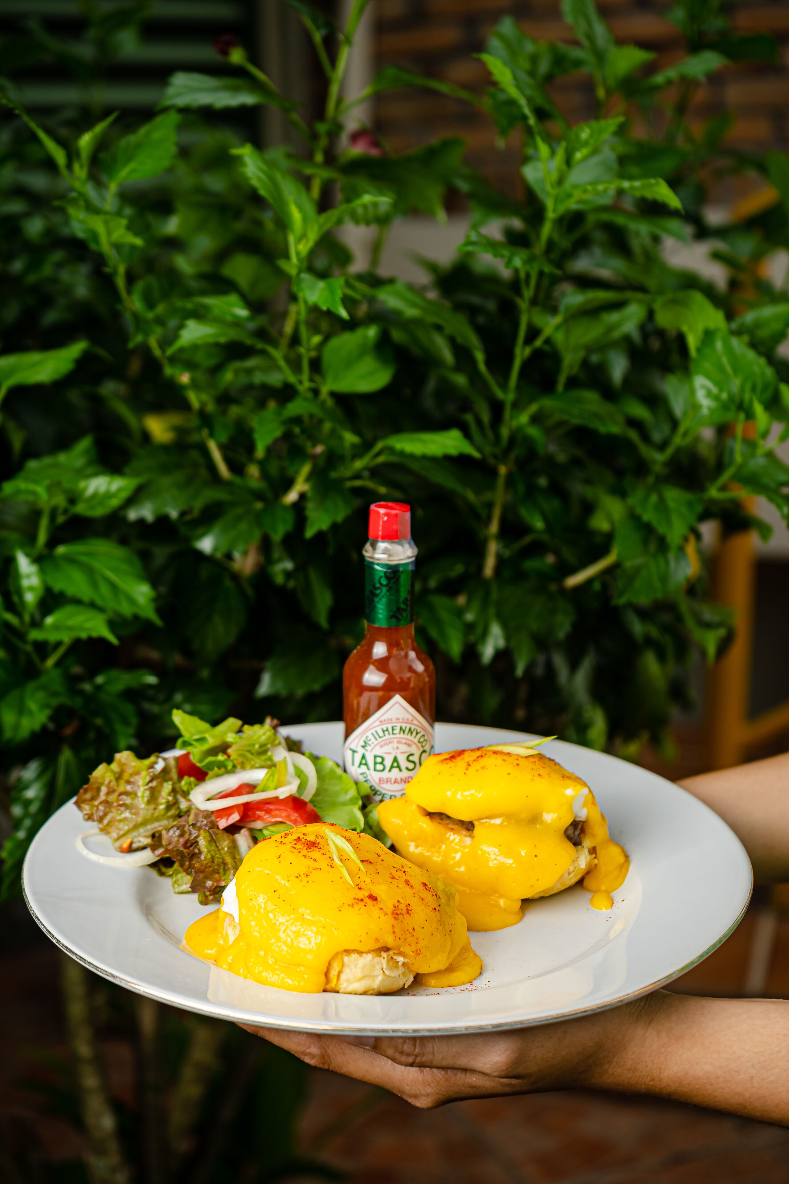 A plate with eggs benedict, a bottle of Tabasco sauce, and a side salad.