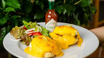 A plate with eggs benedict, a bottle of Tabasco sauce, and a side salad.