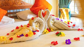 A neatly made bed with a towel arranged in the shape of a swan, surrounded by colorful flowers. - Hotel Deli River (Medan)