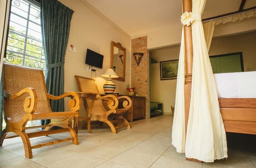 Une chambre d’hôtel avec un lit, deux chaises en bois, une table avec une lampe, un téléviseur et une fenêtre avec des rideaux.
