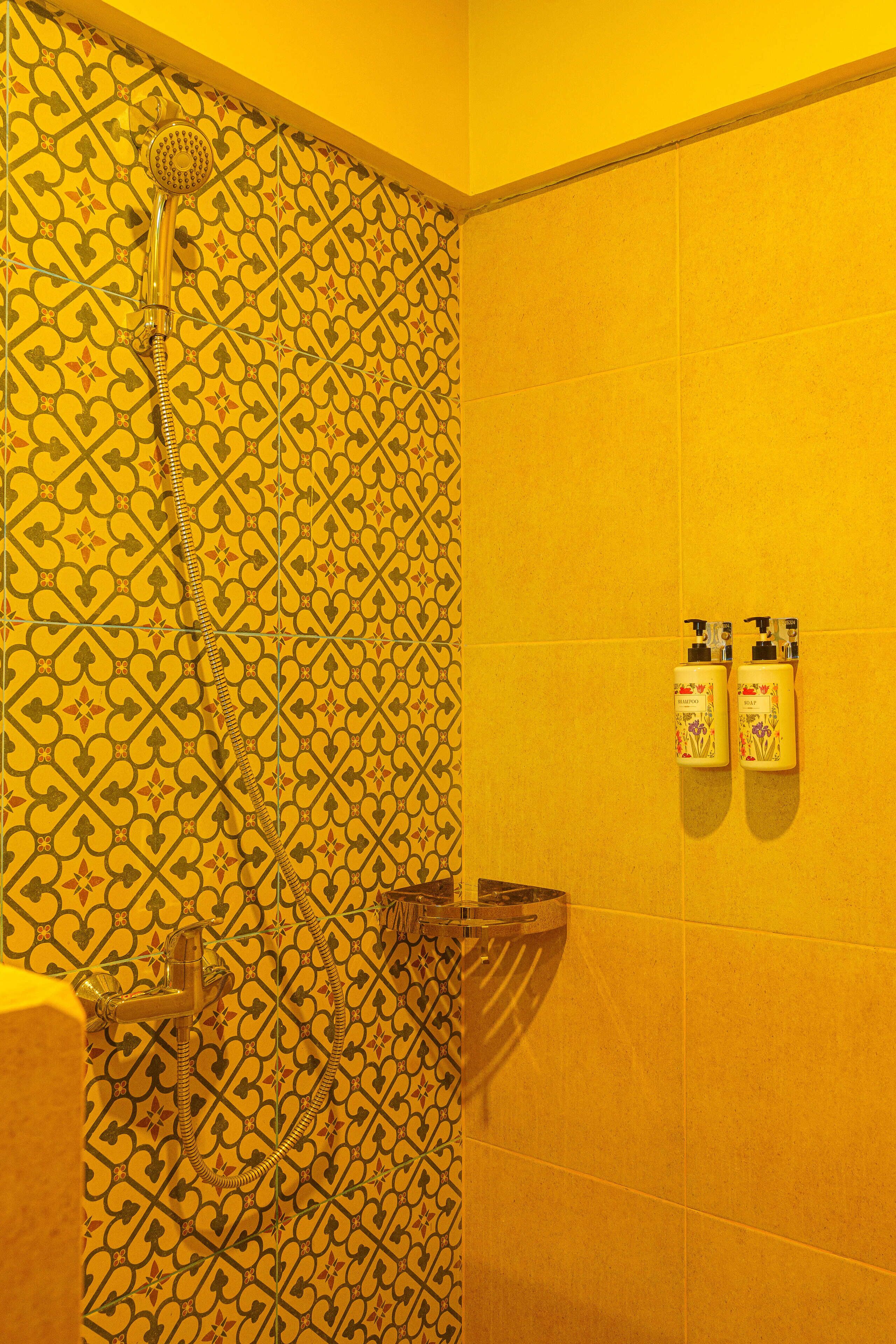 A bathroom with patterned tiles, a shower, and two bottles of shampoo and conditioner on the wall.