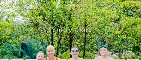 A family in a swimming pool surrounded by lush greenery.