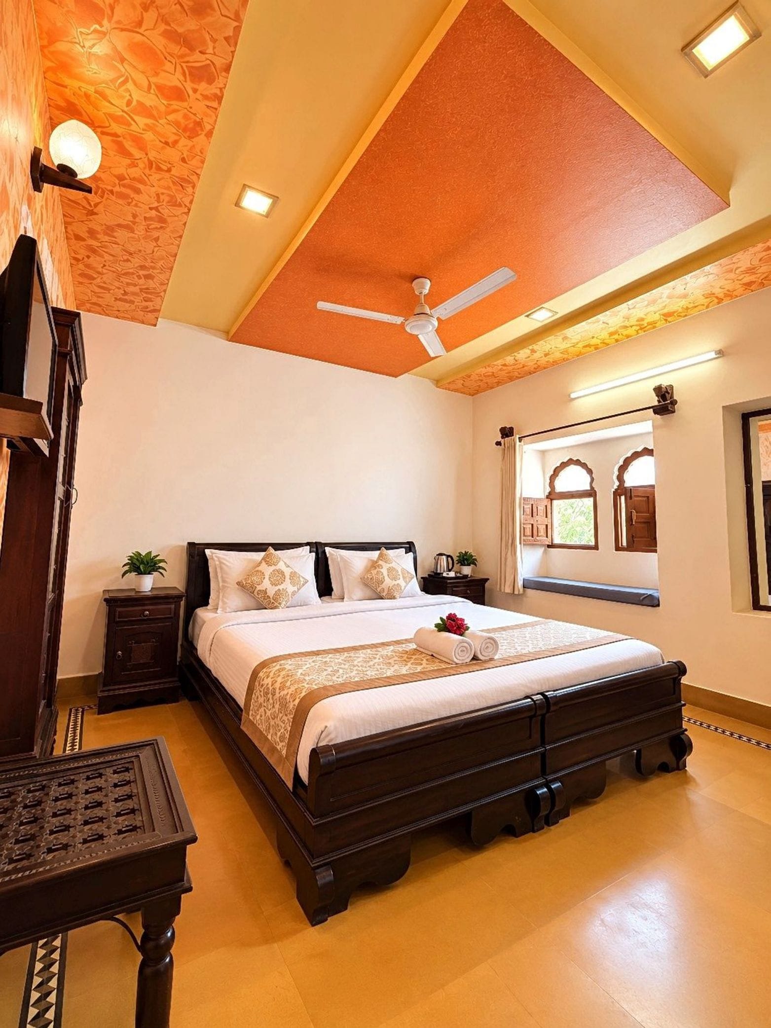 A bedroom with a large bed, a ceiling fan, a nightstand, a table, and a window with a view.