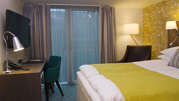 A hotel room with a bed, a desk with a telephone, a chair, a television, and two lamps.