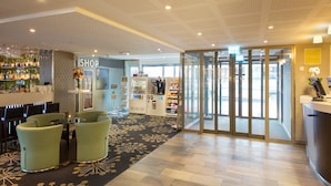 A hotel lobby with a bar area, seating, a shop, and a glass door entrance.