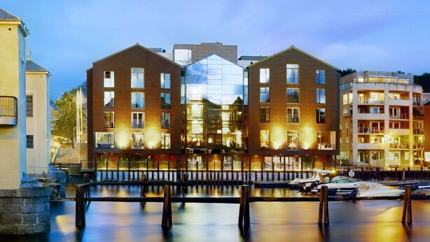 A waterfront hotel with a glass facade, multiple balconies, and a dock with boats.