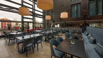 A modern restaurant with high ceilings, large windows, and a mix of seating options including tables and a sofa area.