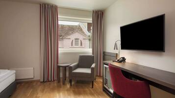 Habitación de hotel con cama, escritorio con computadora, silla, televisor y ventana con cortinas.