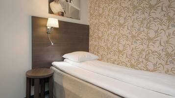A hotel room with a single bed, a small round table, a wall-mounted lamp, and a floral-patterned wallpaper.