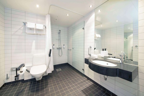 A modern bathroom with a toilet, bidet, shower, and a large mirror above the sink.