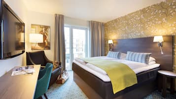 A hotel room with a large bed, a desk with a chair, a television, and a window with curtains.