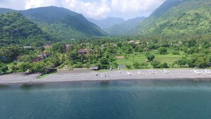 A coastal village with houses, a beach with sun loungers, and lush green hills in the background.