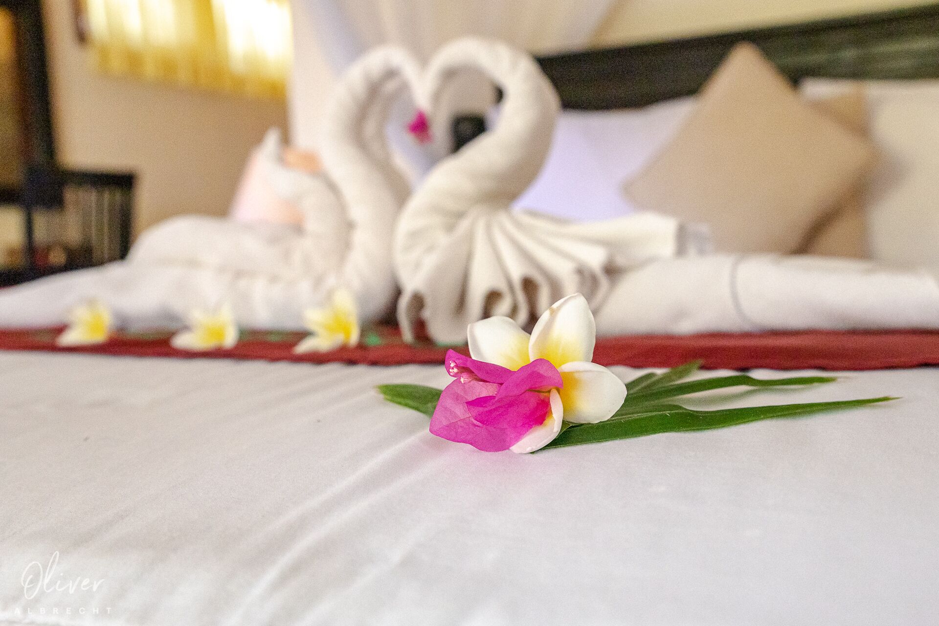 A bed with a heart-shaped towel arrangement and a flower decoration.