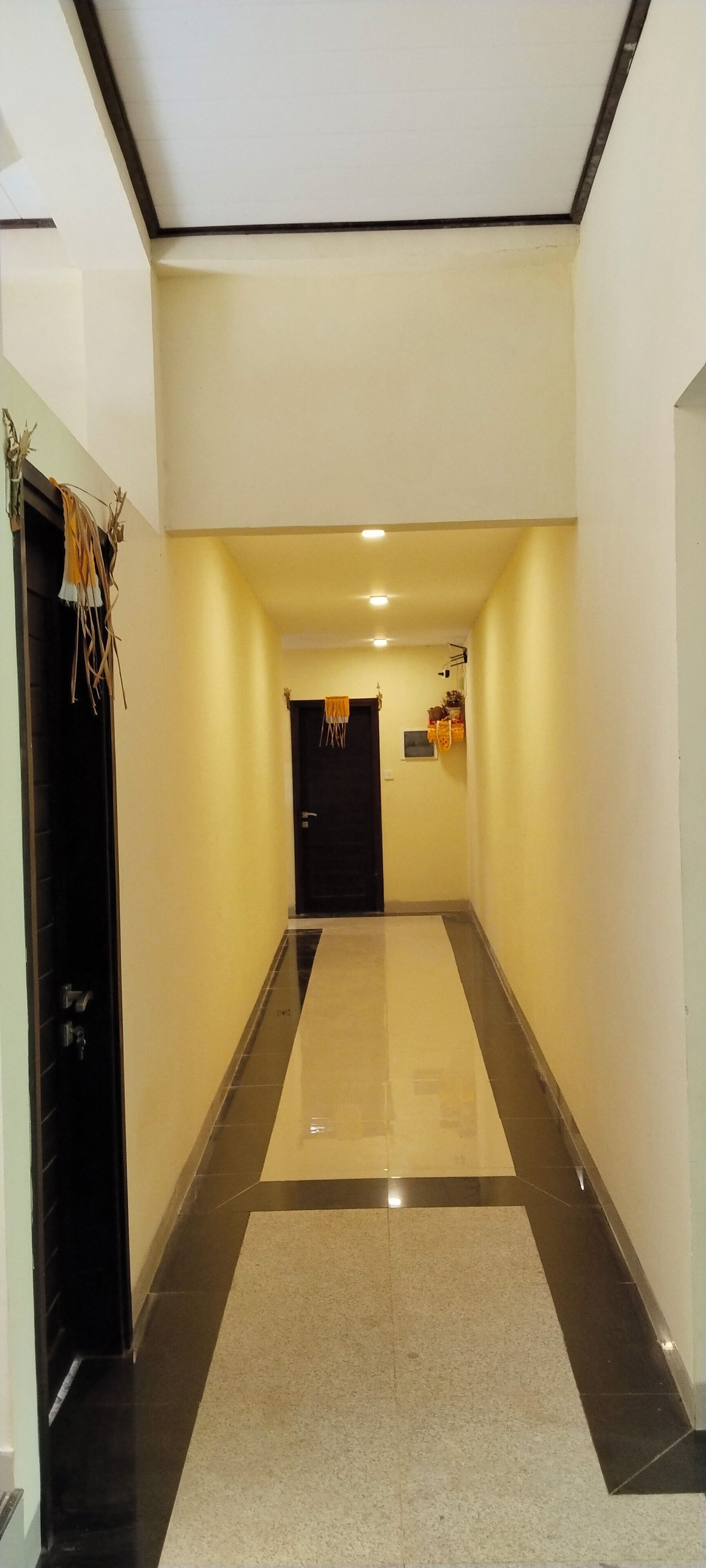 A hallway with a tiled floor, a black door on the left, and a black door at the end.