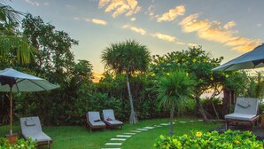 A garden with a stone pathway leading to a seating area with lounge chairs and umbrellas.