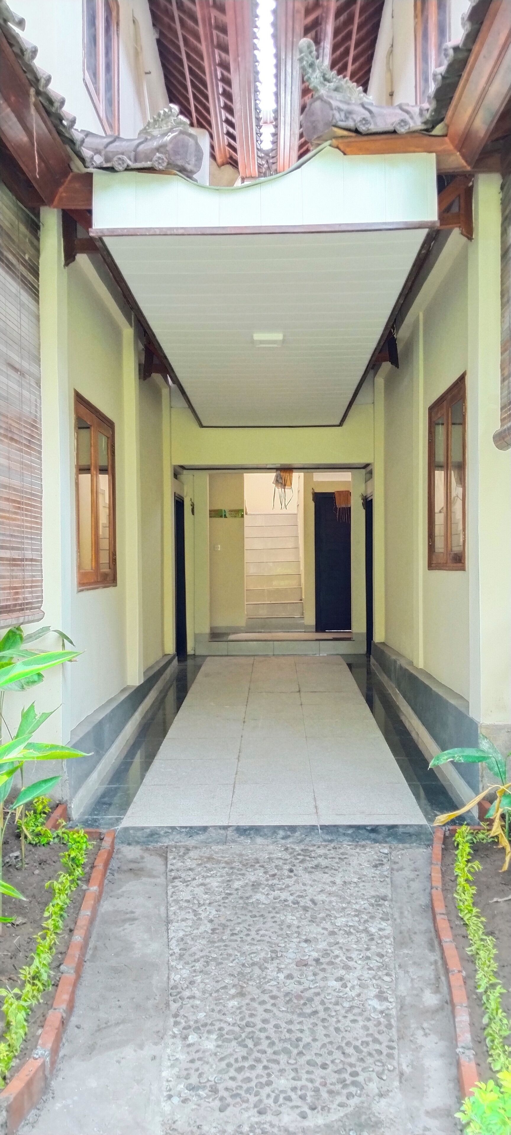 A corridor with a tiled floor, a central rug, and a small garden area with plants.