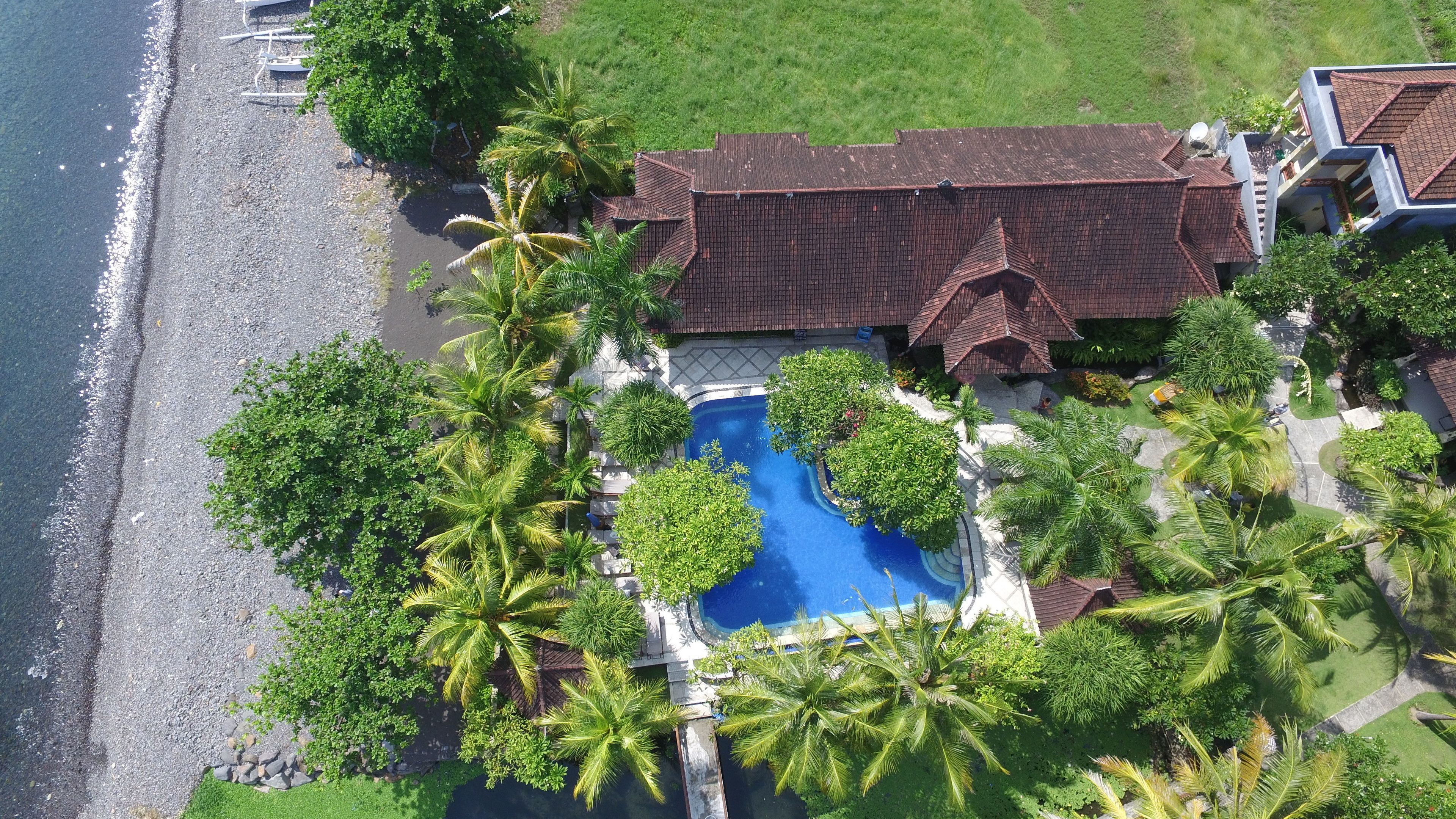 An aerial view of a property with a swimming pool, surrounded by palm trees and a beach.