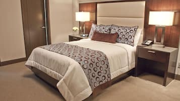 A neatly made bed with a patterned bedspread, two bedside tables with lamps, and a nightstand with a phone.