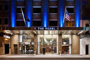 Exterior del hotel The Pearl, con una visible bandera estadounidense, una entrada bien iluminada y un diseño arquitectónico moderno.