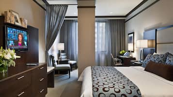 A hotel room with a large bed, a desk, a chair, a TV, and a desk lamp.