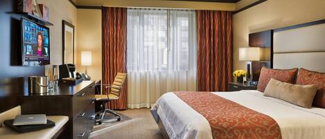 Una habitación de hotel con una cama grande, un escritorio con una computadora portátil, un televisor y una ventana con cortinas.