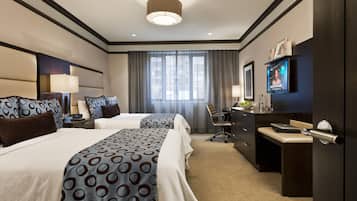 Een hotelkamer met twee bedden, een bureau, een stoel, een televisie en een groot raam met gordijnen.
