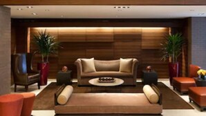 Um lobby moderno com um conjunto de sofás, duas plantas em vasos e uma mesa de centro.