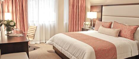 A hotel room with a large bed, a desk with a chair, a nightstand, and a lamp.