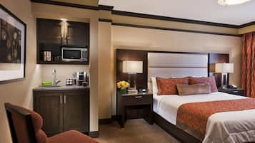 A hotel room with a bed, a desk with a lamp, a microwave, and a chair.