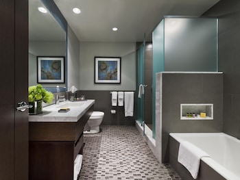 A hotel room with a bed, desk, chair, TV, and a view of the outside. at The Pearl New York