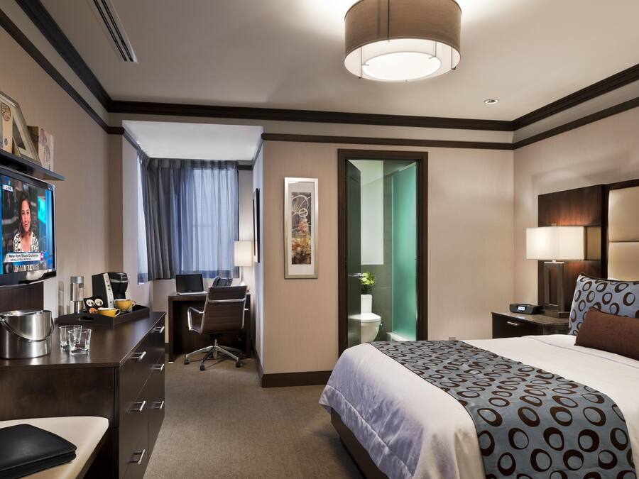 Camera d'albergo con un letto, una scrivania, una sedia, televisione e bagno parzialmente visibile da una porta aperta.