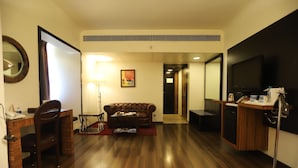 Een hotelkamer met een houten vloer, een bank, een bureau met stoel, een televisie en een spiegel.