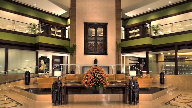 Een ruime lobby met een centraal zitgedeelte, een groot decoratief bloemarrangement en een statige trap.