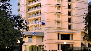 Een meerlaags hotel met een platte gevel, diverse balkons en een centrale ingang met een lamp.