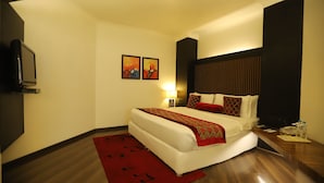 Een hotelkamer met een groot bed, een houten vloer, een rood tapijt en twee schilderijen aan de muur.