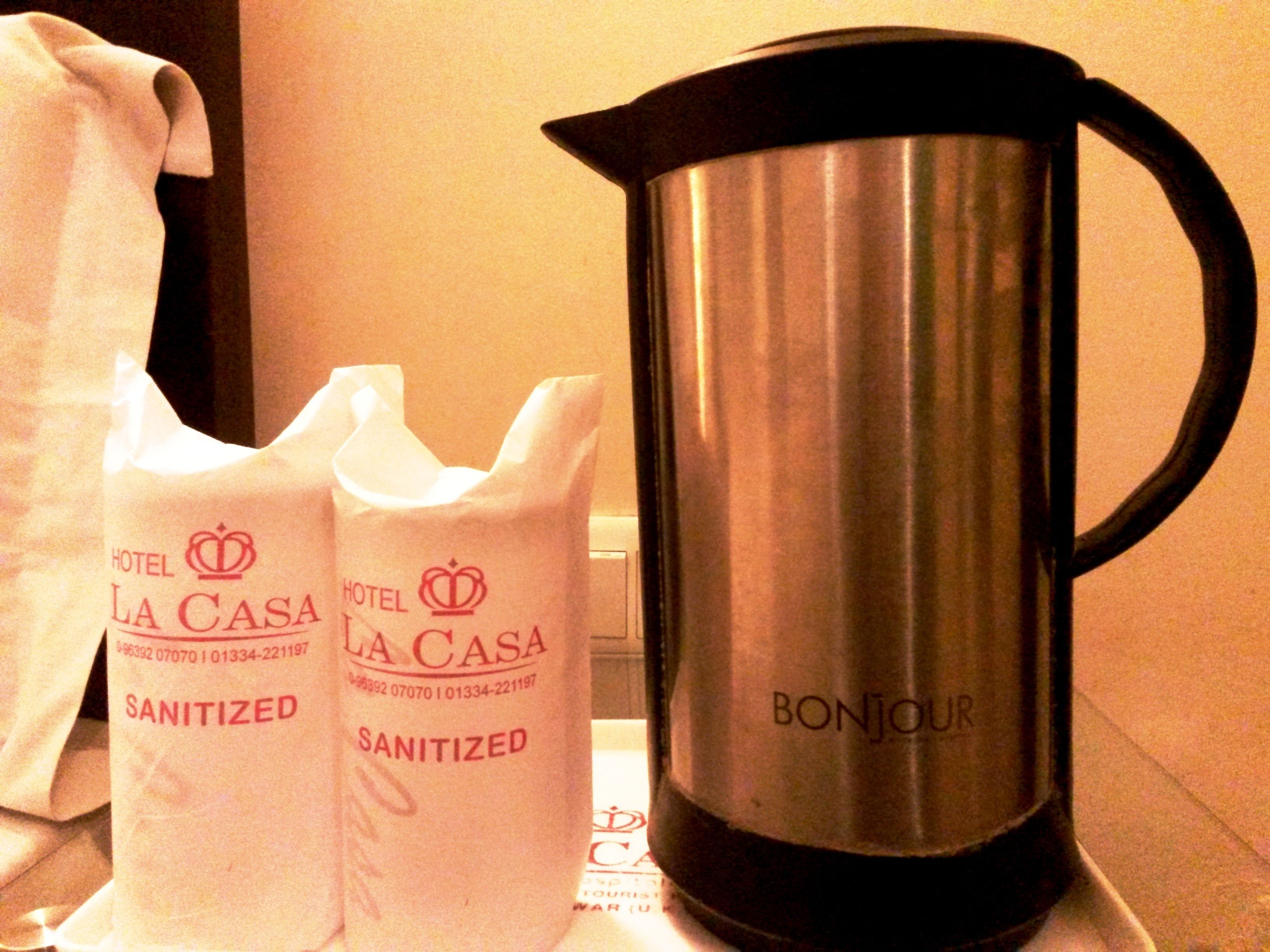 A stainless steel pitcher with "BONJOUR" and two white bags labeled "SANITIZED" from Hotel La Casa.