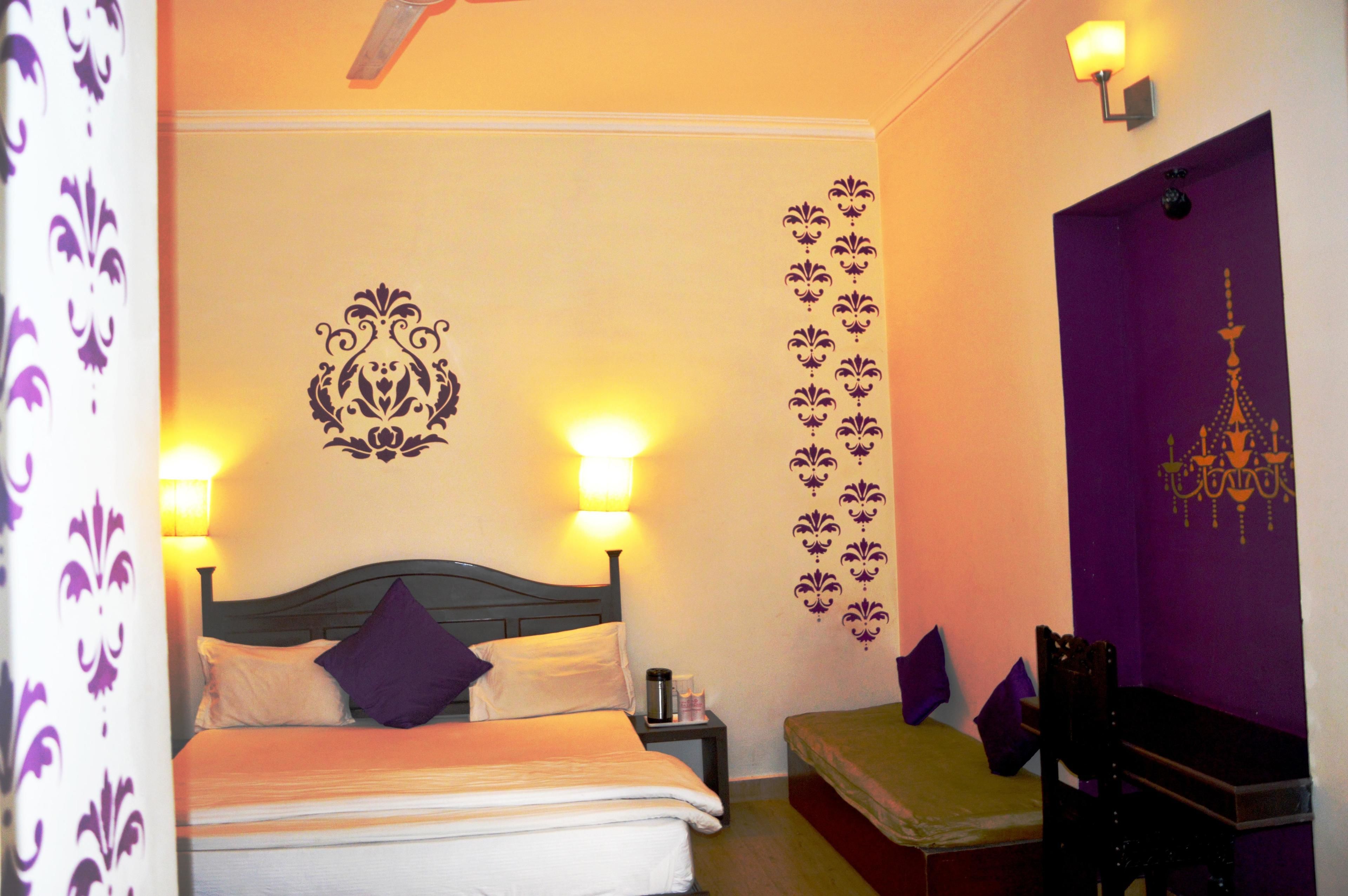 A hotel room with a bed, two bedside lamps, a nightstand, a chair, and a purple door.
