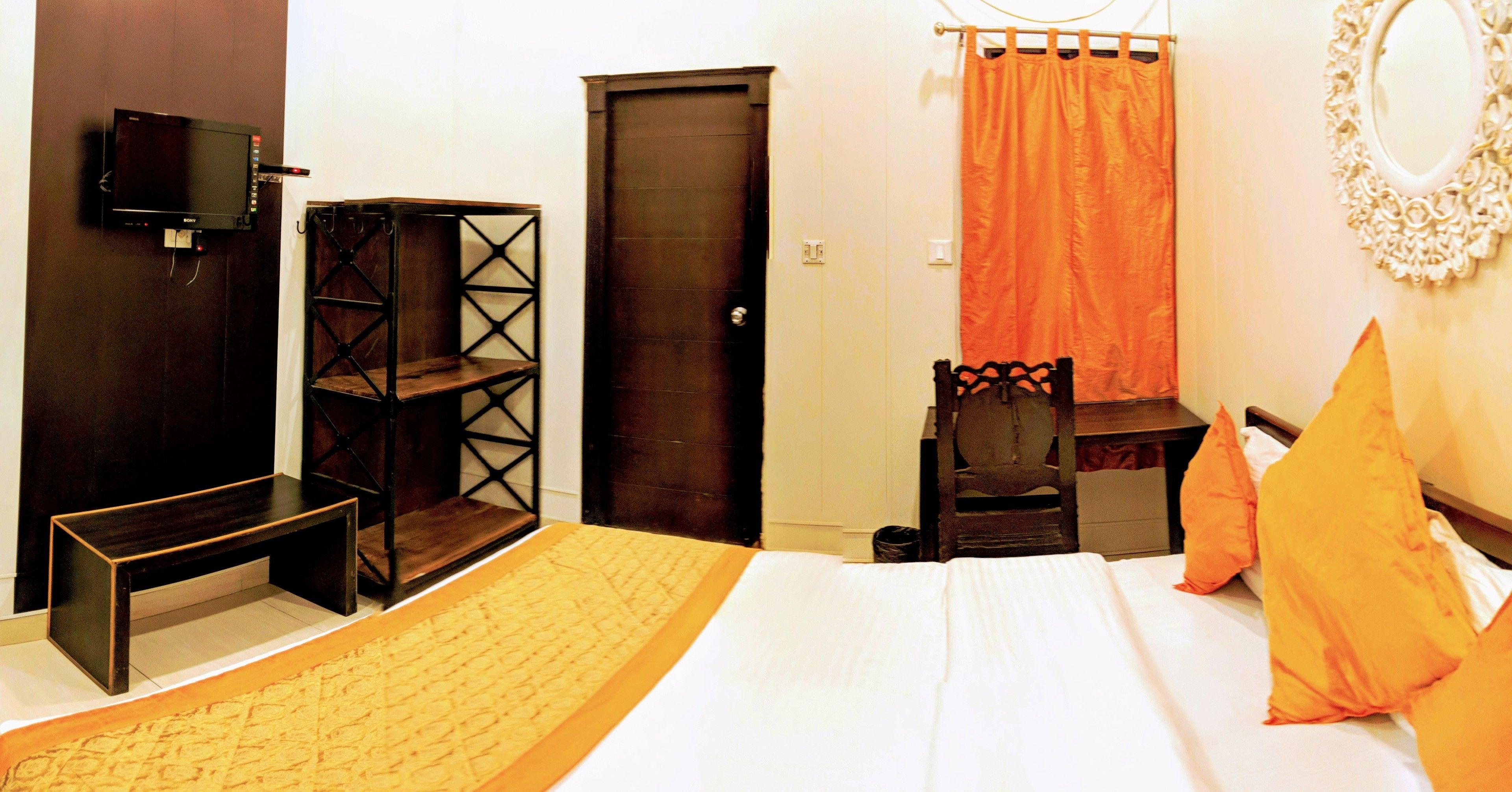 Ein Schlafzimmer mit Bett, Sessel, Schreibtisch, Fernseher und einer Tür.