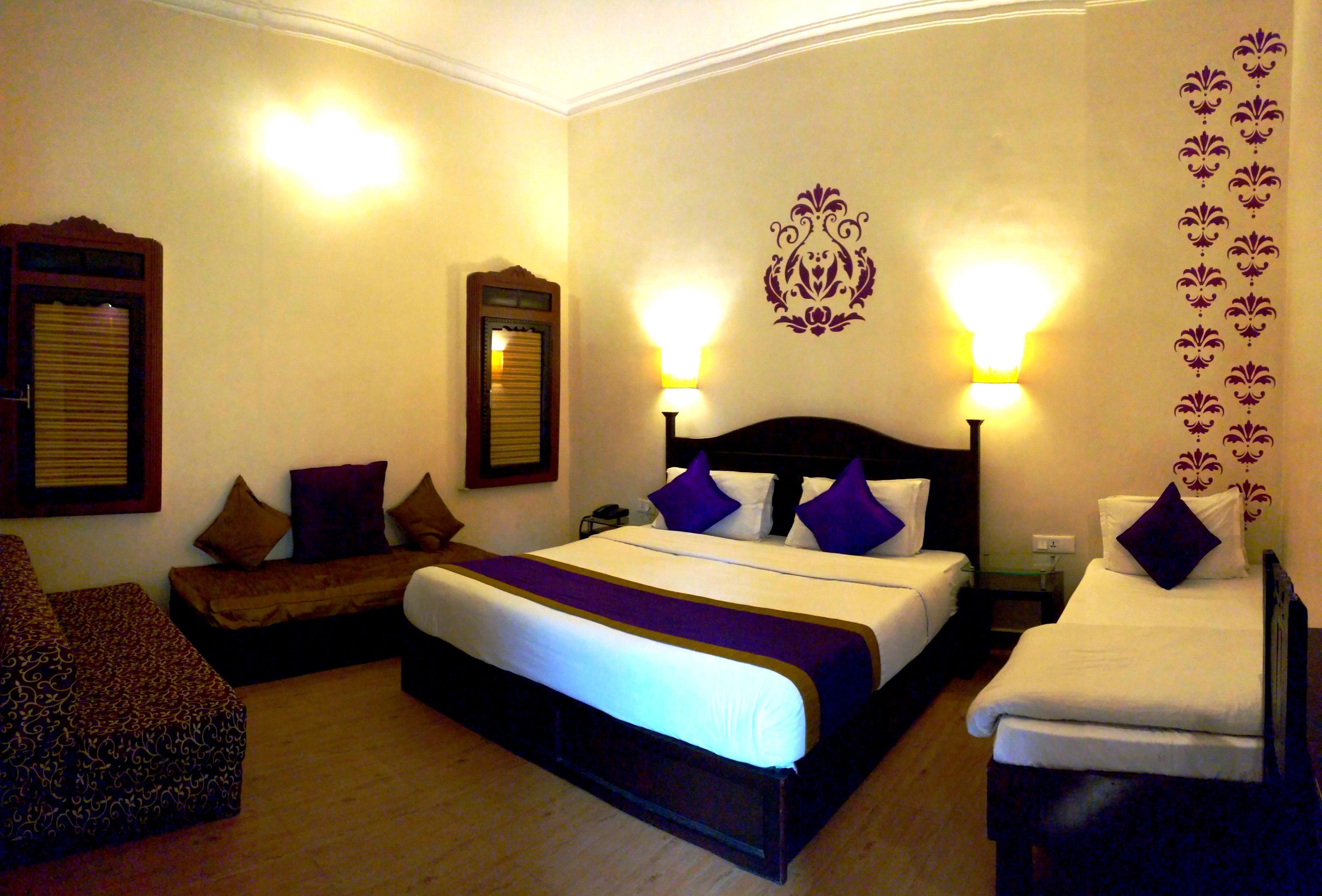 A hotel room with a large bed, two bedside tables, a nightstand, a sofa, and a patterned armchair.