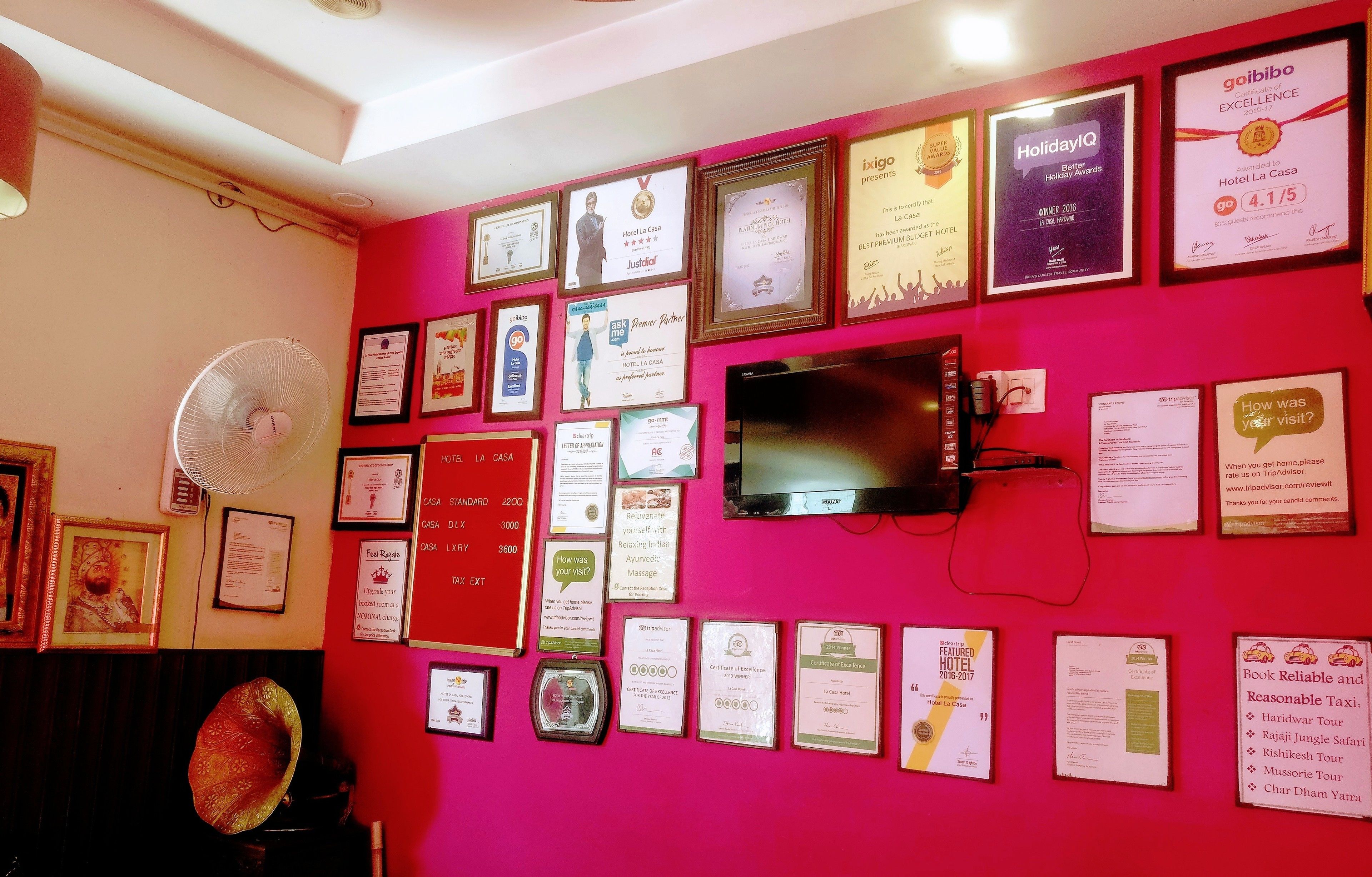 Una pared con varios premios y certificados enmarcados, un televisor y un ventilador.