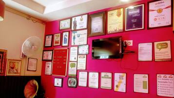 Una pared con varios premios y certificados enmarcados, un televisor y un ventilador.