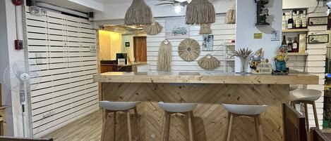 A bar area with wooden stools, a counter, and hanging light fixtures.