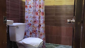 A bathroom with a toilet, a sink, a shower curtain with a floral pattern, and a tiled floor.