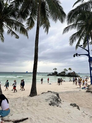 A beach with palm trees, people walking, and a rocky outcrop in the background. - La Bella Casa de Boracay (Boracay Island)