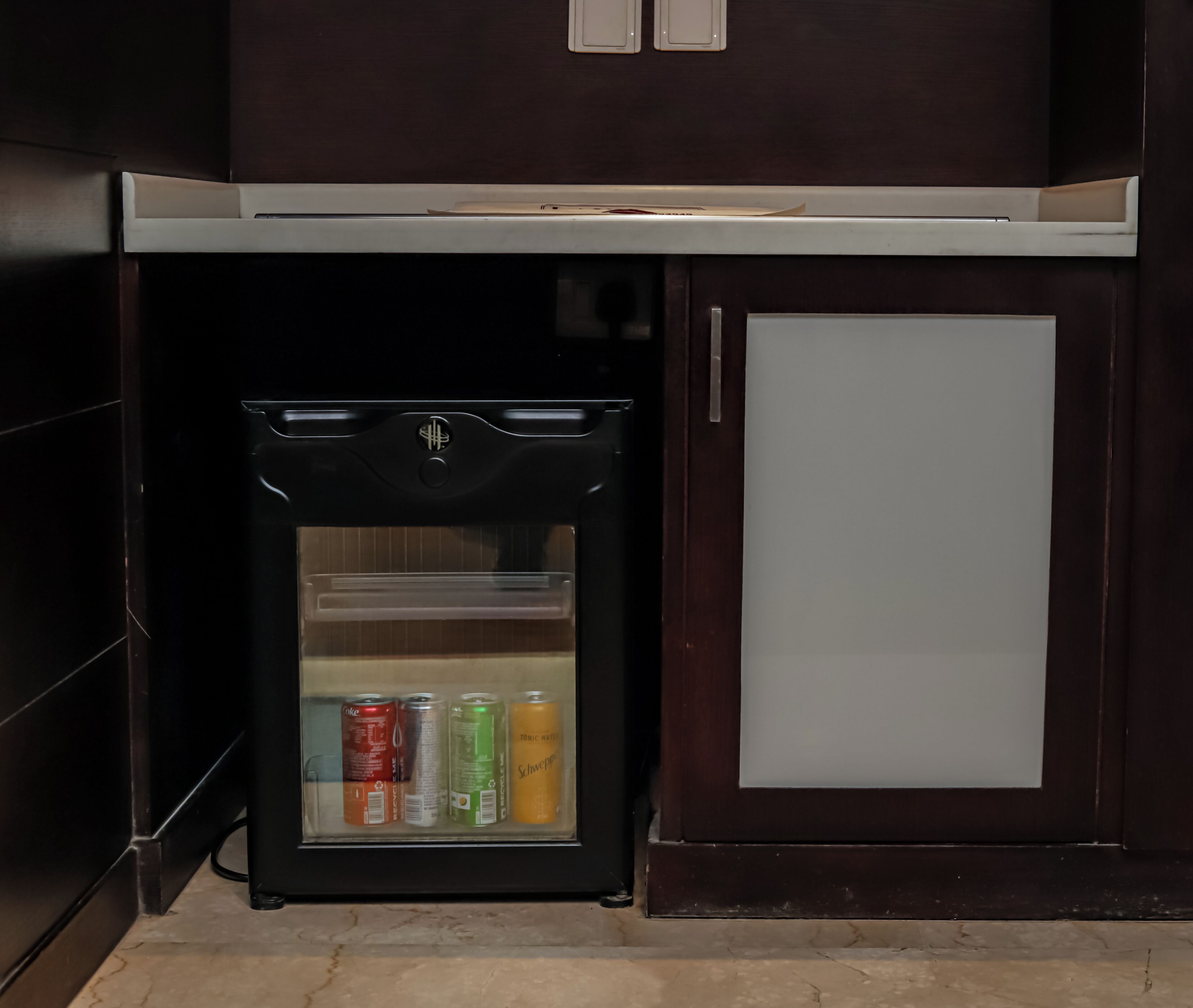 A small black refrigerator with a glass door, containing several cans of beverages.