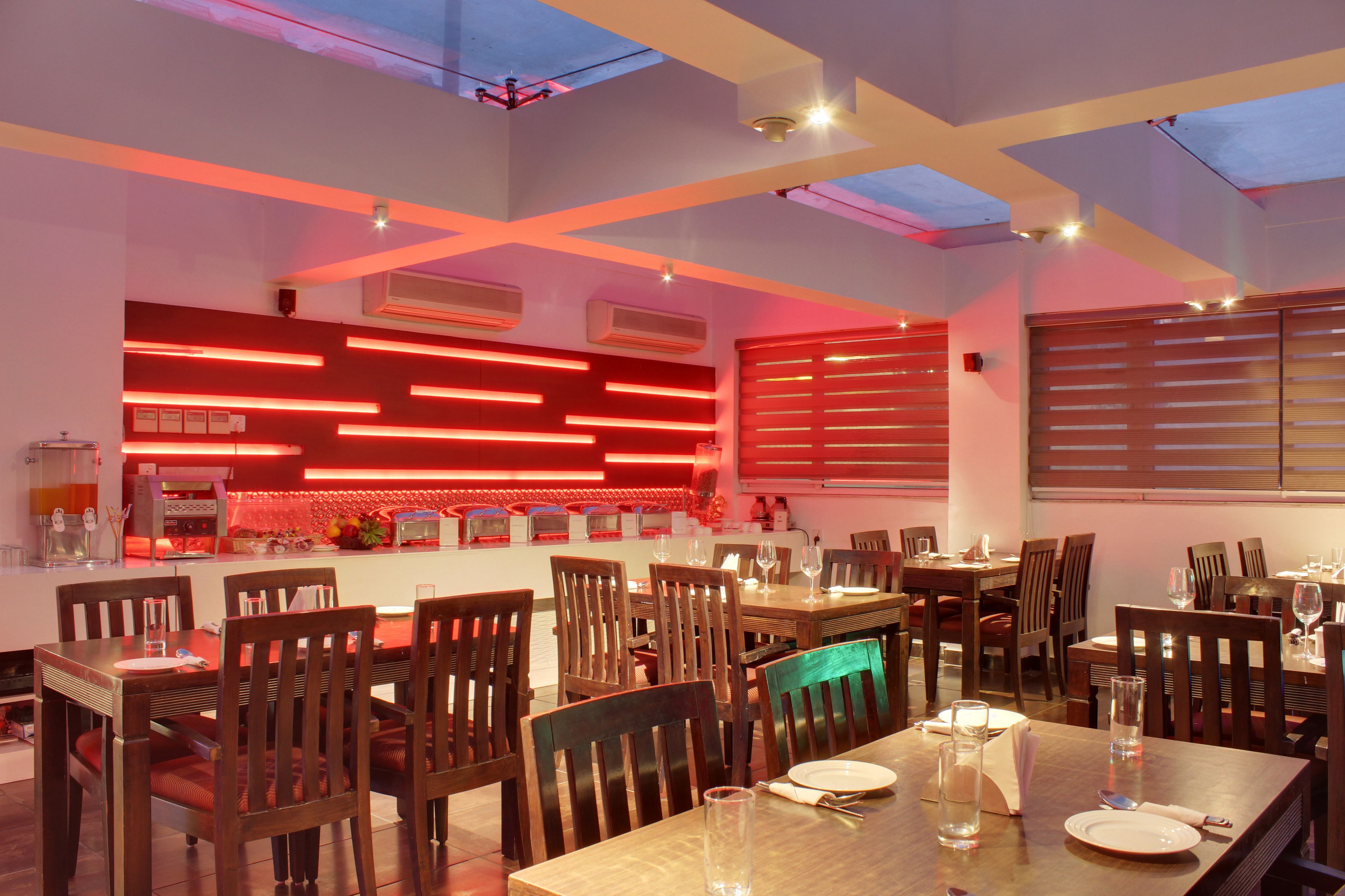 Un restaurante con una decoración moderna, que presenta una larga mesa de comedor, múltiples sillas y una zona de cocina con iluminación roja.