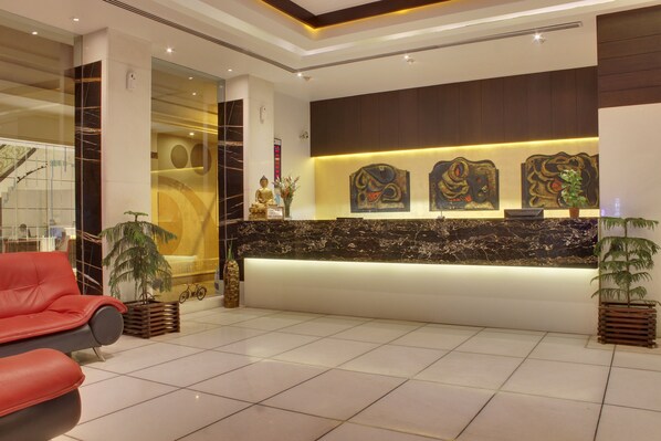 A modern reception area with a marble counter, a red sofa, and decorative wall art. - Hotel Godwin Deluxe (New Delhi)
