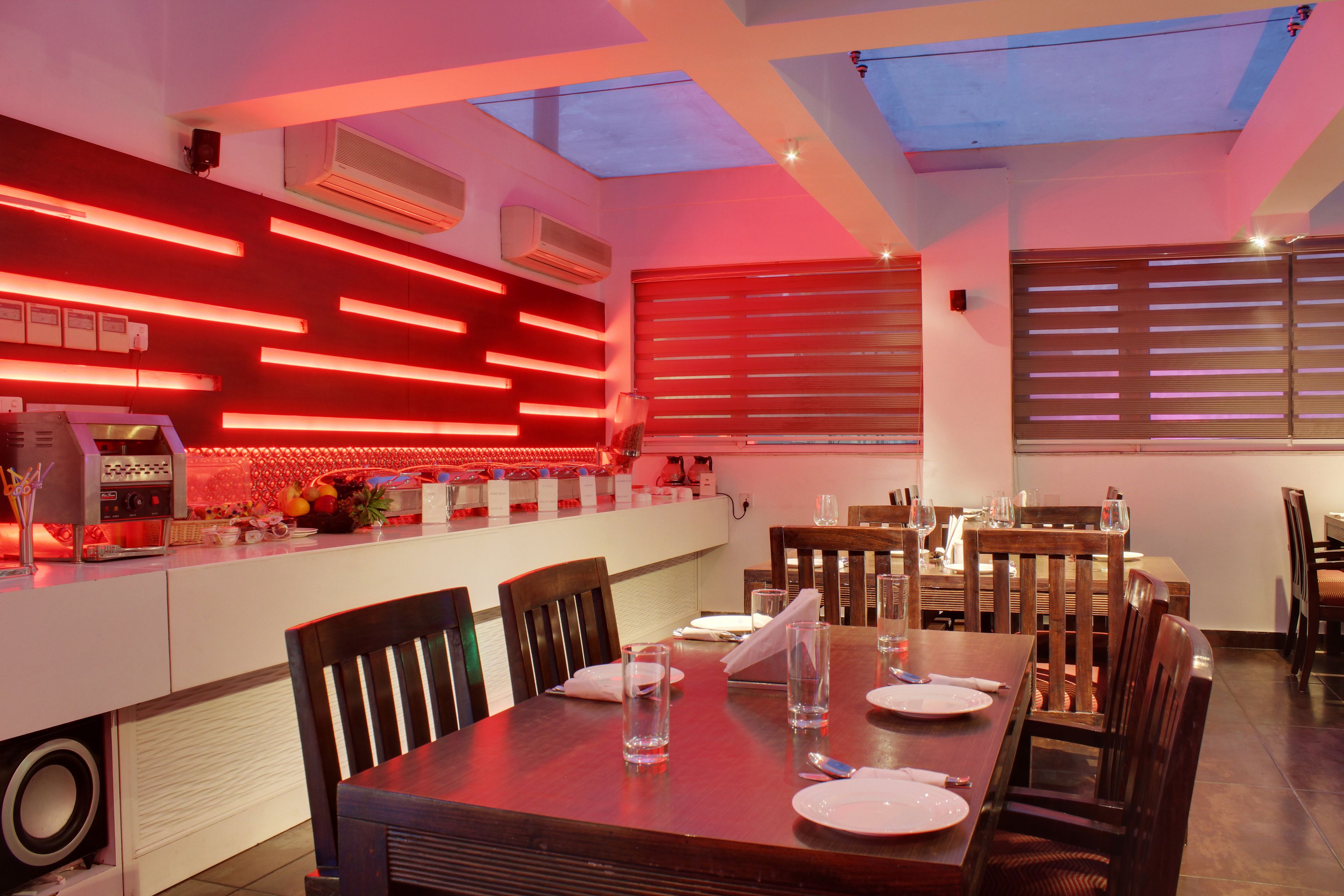 Un comedor moderno con una mesa larga dispuesta para dos, sillas de madera y una zona de bar con iluminación roja.