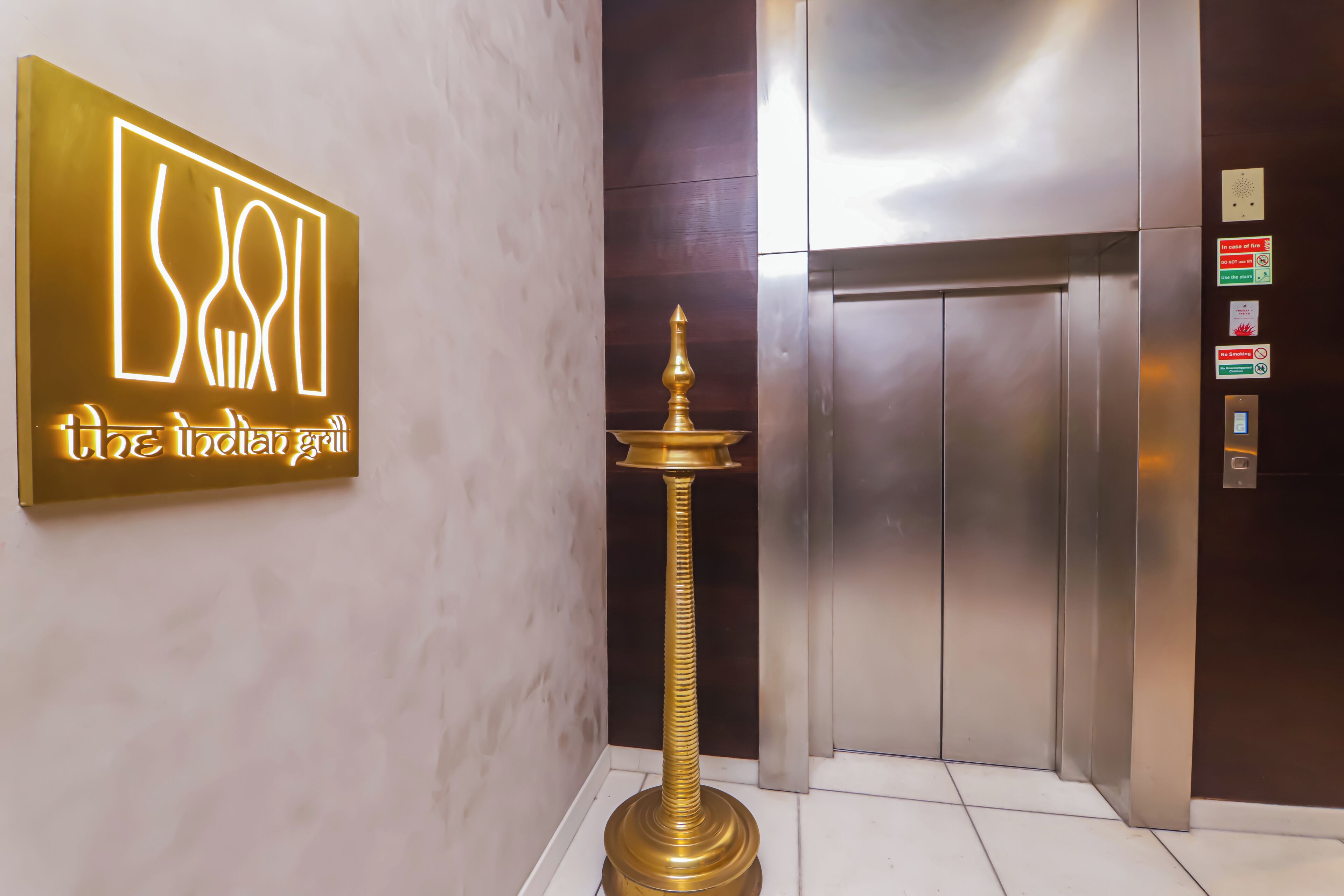 Un ascenseur au design moderne, une enseigne pour le restaurant « The Indian Grill » et une lampe en laiton.
